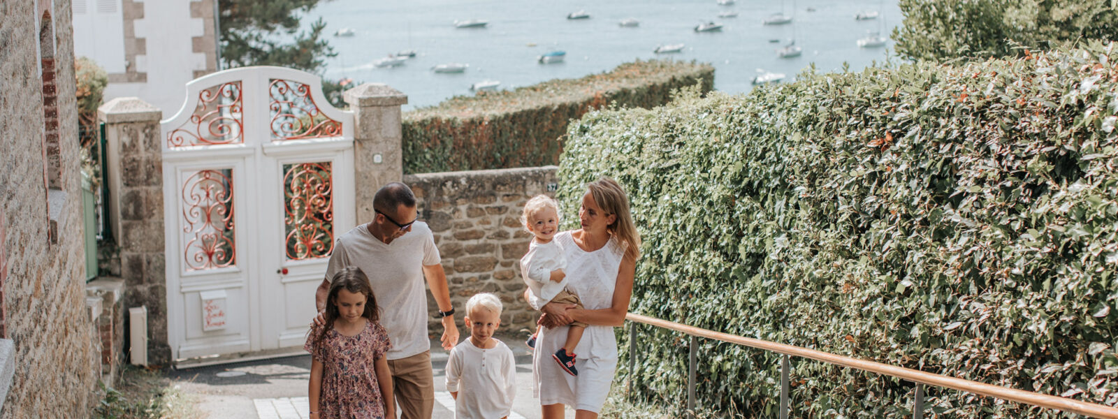 Une famille se promène sur le boulevard de la mer à Saint-Briac. Ils remontent la rue, et derrière eux, on peut apercevoir la mer étendu sous un ciel dégagé