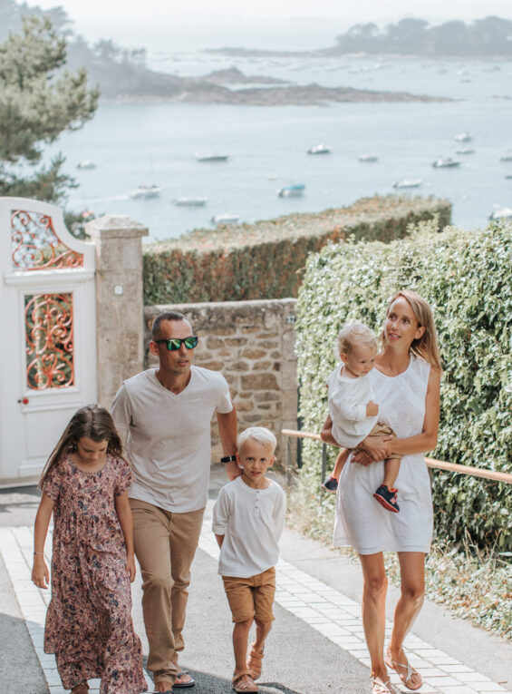 Un couple et ses trois enfants se promènent sur le boulevard de la mer à Saint-Briac. Ils remontent la rue, et derrière eux, on peut apercevoir la mer étendu sous un ciel dégagé