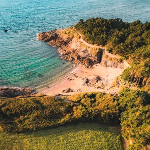 Vue d'une jolie crique à Dinard, sur la Côte d'Émeraude au coucher du soleil. La végétation surplombe la plage de sable fin. Crédit photo : Lezbroz