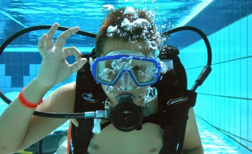 Un plongeur fait un signe sous l'eau dans une piscine. Apprenez la plongée avec Nautilus Dive Center à Dinard et participez à des sorties de Plongée Sous Marine en Bretagne.