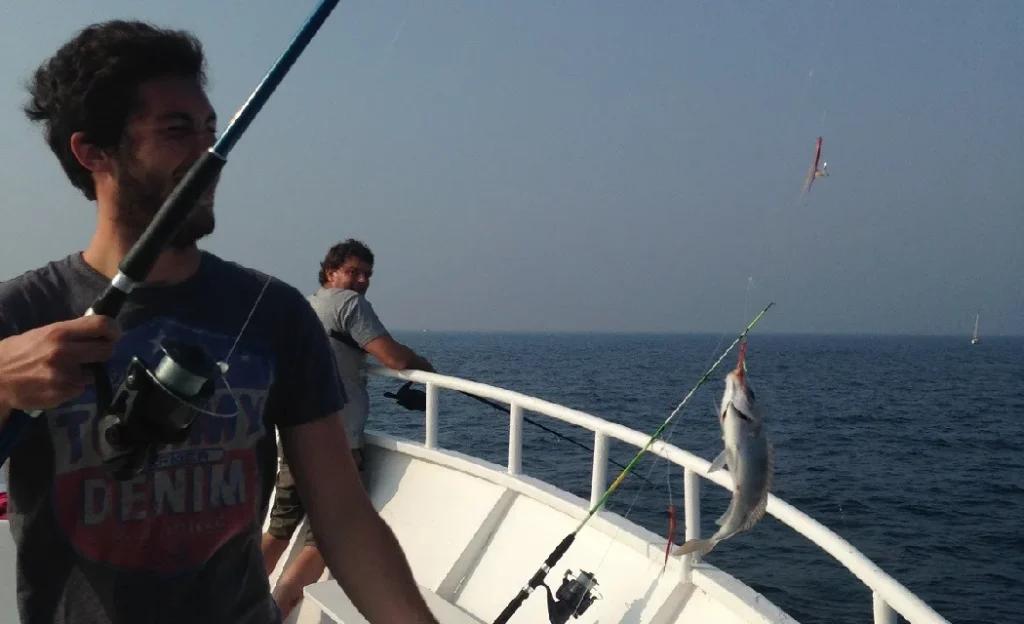 Deux hommes tiennent une canne à pêche sur un bateau lors d'une activité pêche en mer organisée par la Compagnie Corsaire au départ de Dinard et Saint-Malo.