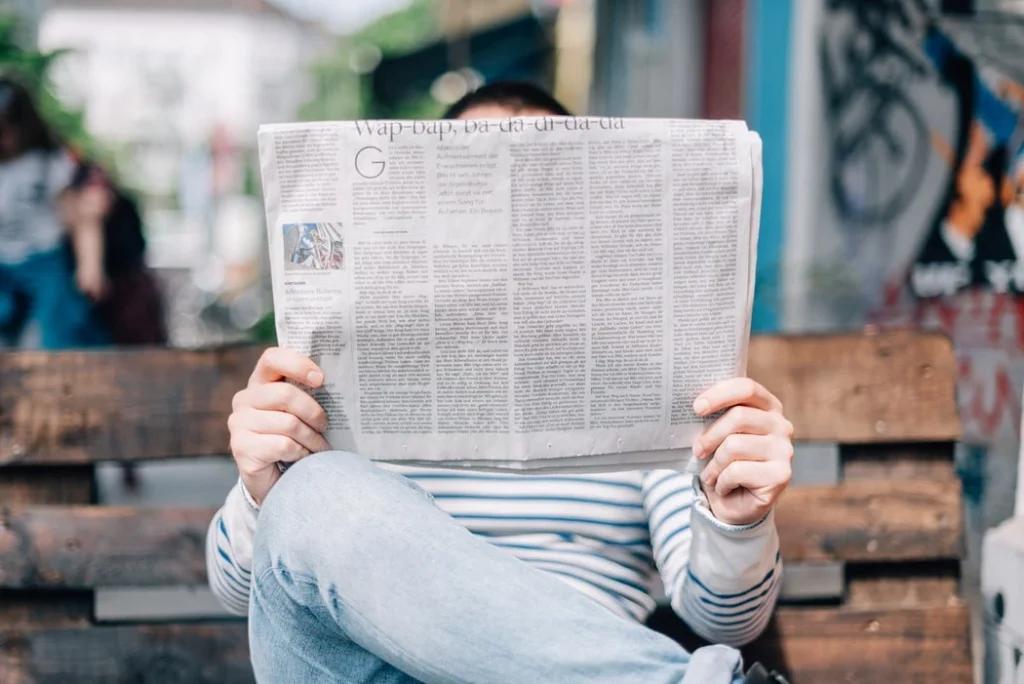 Un homme assis sur un banc lit son journal. Espace pro revue de presse