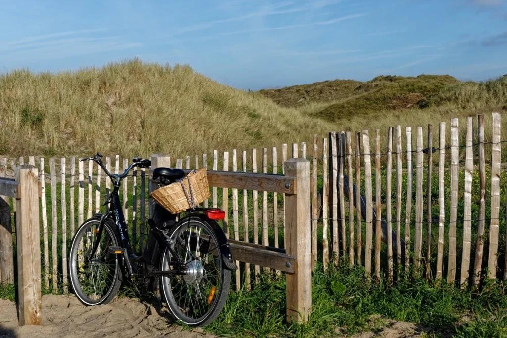 Un vélo est attaché à une barrière en bois, le long de dunes sableuses sur la Côte d'Émeraude.