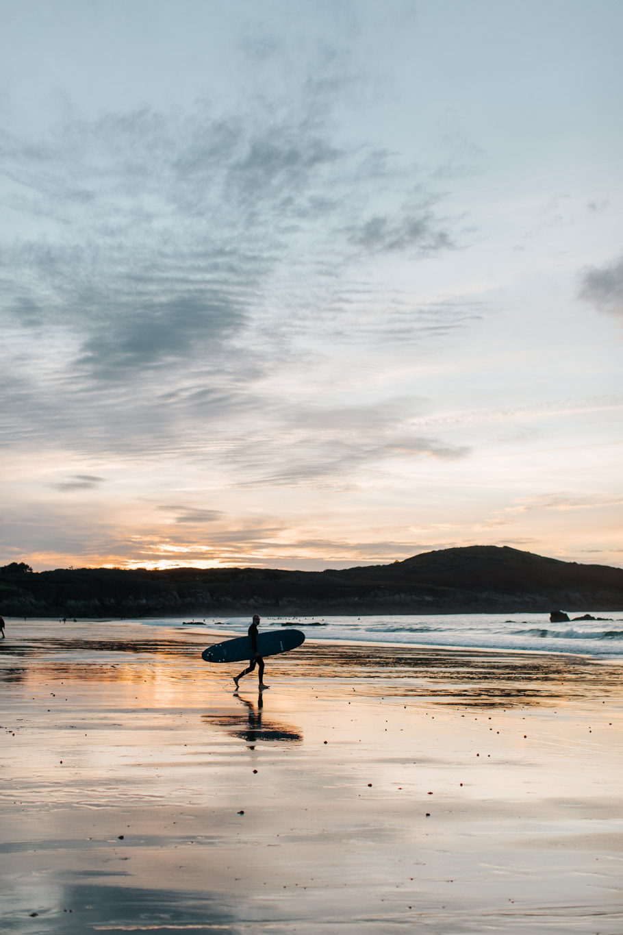 Un surfeur se dirige vers la mer au coucher du soleil sur la plage de Longchamp, spot de surf de la côte nord de la Bretagne, située sur les communes de Saint-Lunaire et Saint-Briac-sur-Mer.