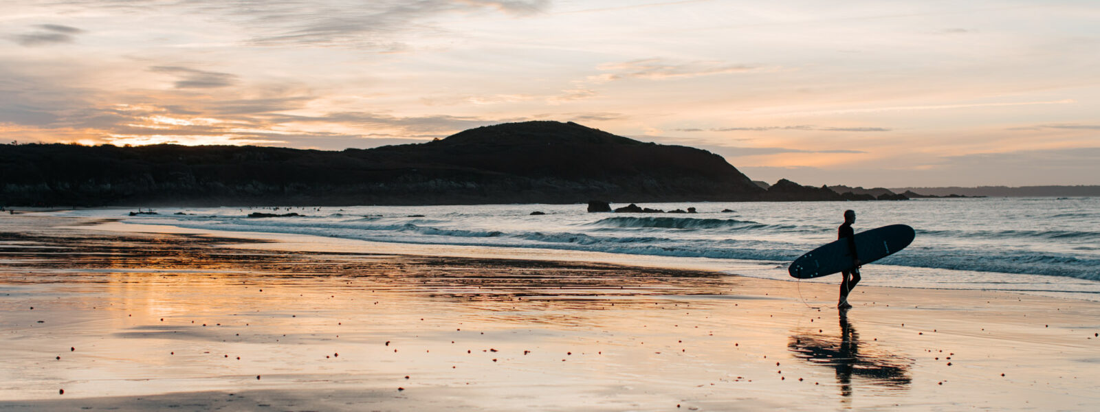 Sur la Plage de Longchamp Saint-Lunaire un homme en combinaison se dirige vers la mer. Les lumières de la fin de journée sont douces