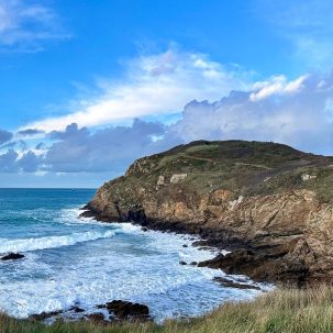 Vue de la Pointe de la Garde Guérin à Saint Briac Sur Mer depuis l'ouest. Pointe rocheuse avec une végétation basse, entourée de la mer. Des vagues s'échouent en contrebas. Crédit photo Charlotte Longépé