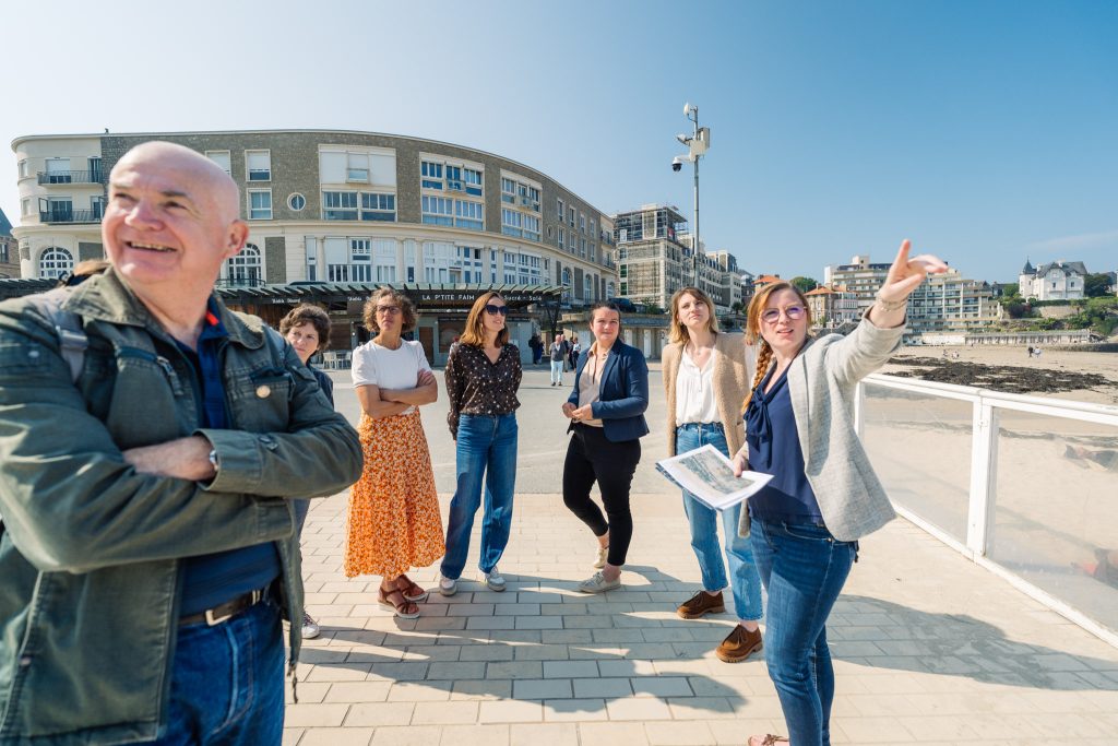 Un groupe de personnes suit une visite guidée avec une guide conférencière à Dinard au bord de la plage de l'Écluse. Crédit photo : Jérémy JEHANIN
