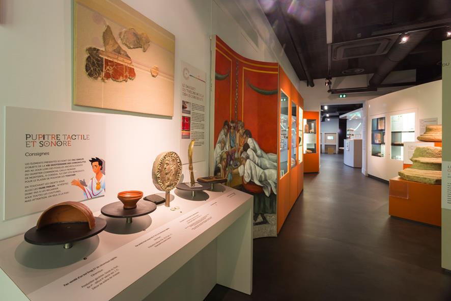 Photo d'une salle du musée Archéomusée Coriosolis. La structure blanche et organe présente des objets gallo-romains et du texte explicatif pour les visiteurs.