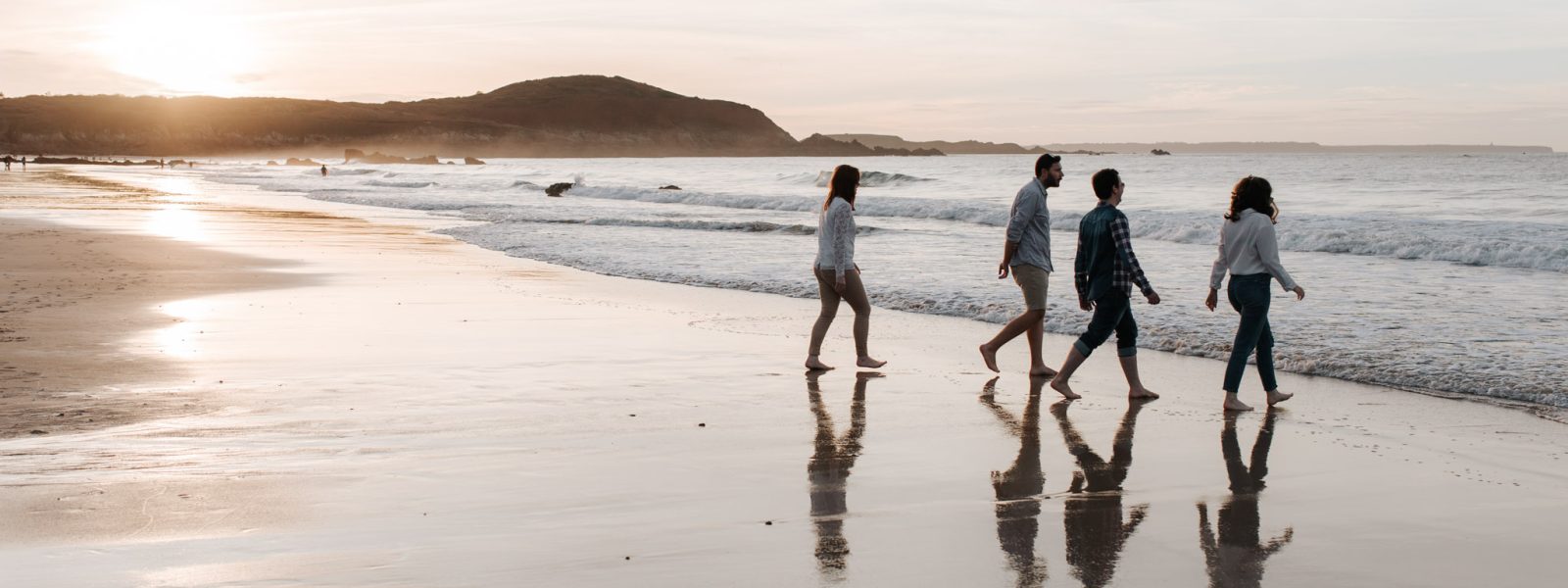 Quatre personnes marchant pieds nus sur une plage au coucher du soleil, au bord de la mer, à Saint-Lunaire, plage de Lonchamp.