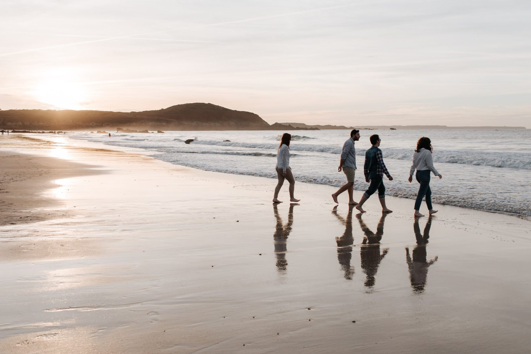 Quatre personnes marchant pieds nus sur une plage au coucher du soleil, au bord de la mer, à Saint-Lunaire, plage de Lonchamp.