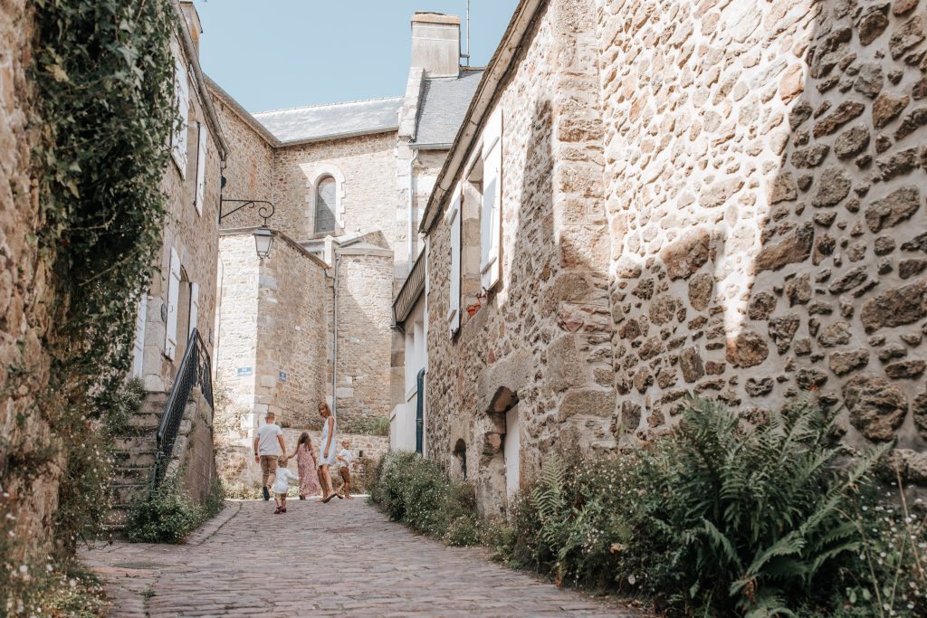 Famille se promenant dans une ruelle pavée bordée de maisons en pierre dans le village de Saint-Briac-sur-Mer.