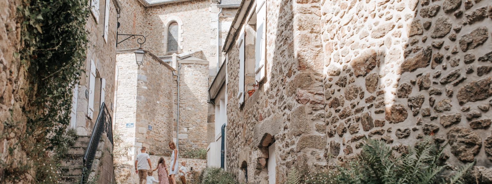 Famille se promenant dans une ruelle pavée bordée de maisons en pierre dans le village de Saint-Briac-sur-Mer.
