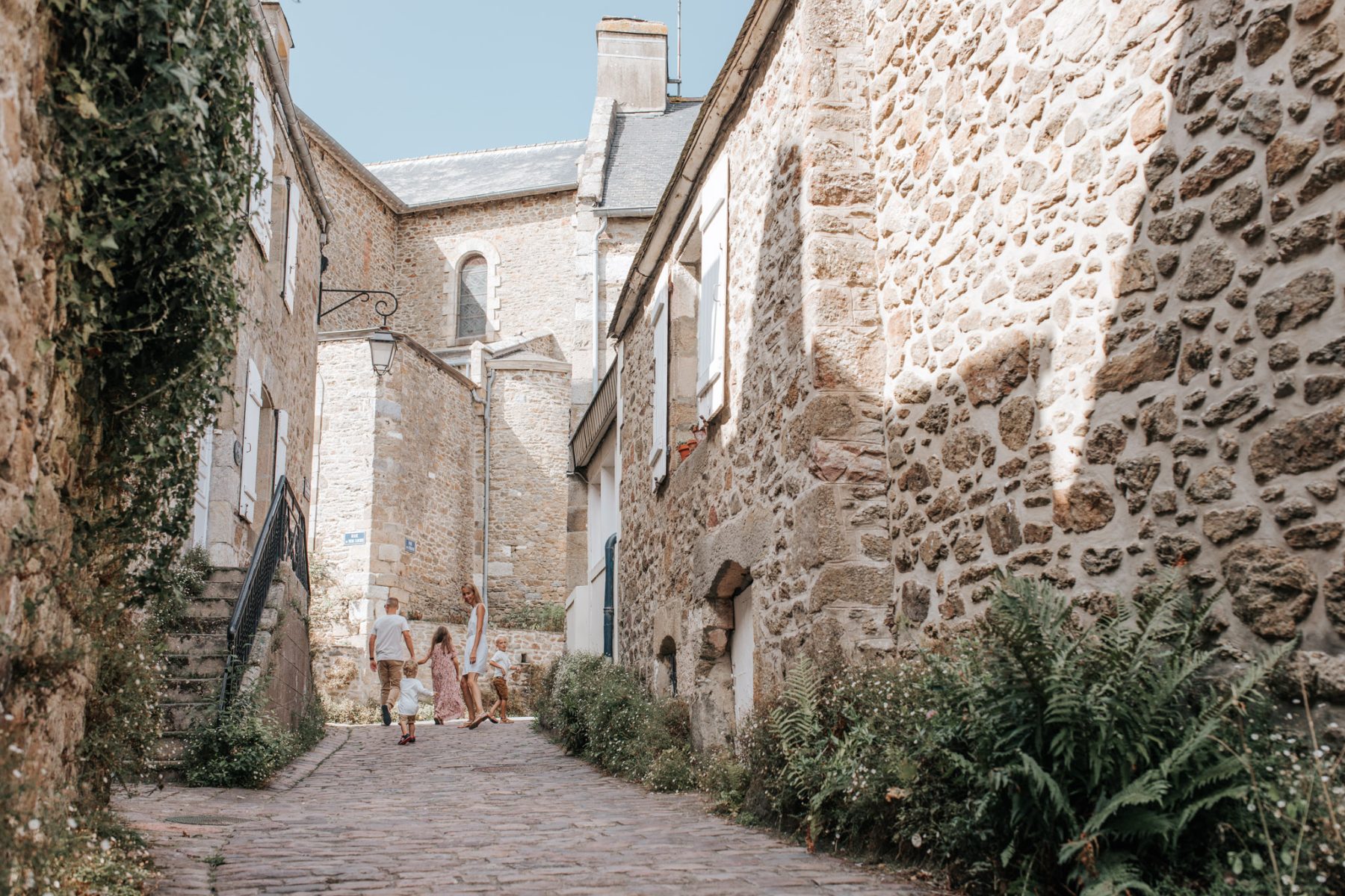 Famille se promenant dans une ruelle pavée bordée de maisons en pierre dans le village de Saint-Briac-sur-Mer.